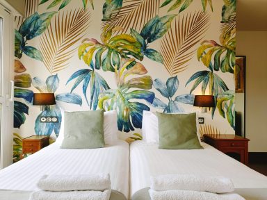 Frente Habitación 102 Habitación con dos camas individuales, decorada con papel pintado de hojas tropicales.