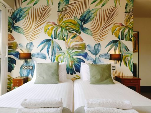 Habitación con dos camas individuales, decorada con papel pintado de hojas tropicales.