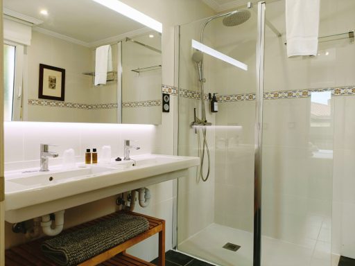 Baño moderno con ducha, lavabo doble y toallas blancas colgadas. Decoración minimalista.