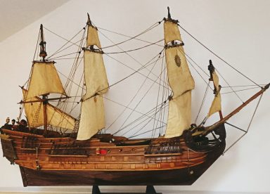 Fragata antigua Modelo de barco antiguo con velas y detalles de madera en un fondo claro.