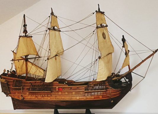 Modelo de barco antiguo con velas y detalles de madera en un fondo claro.