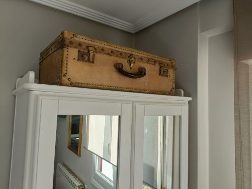 Maleta antigua de color claro sobre un mueble blanco con espejos.
