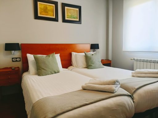 Habitación con dos camas individuales, sábanas blancas y decoración minimalista.